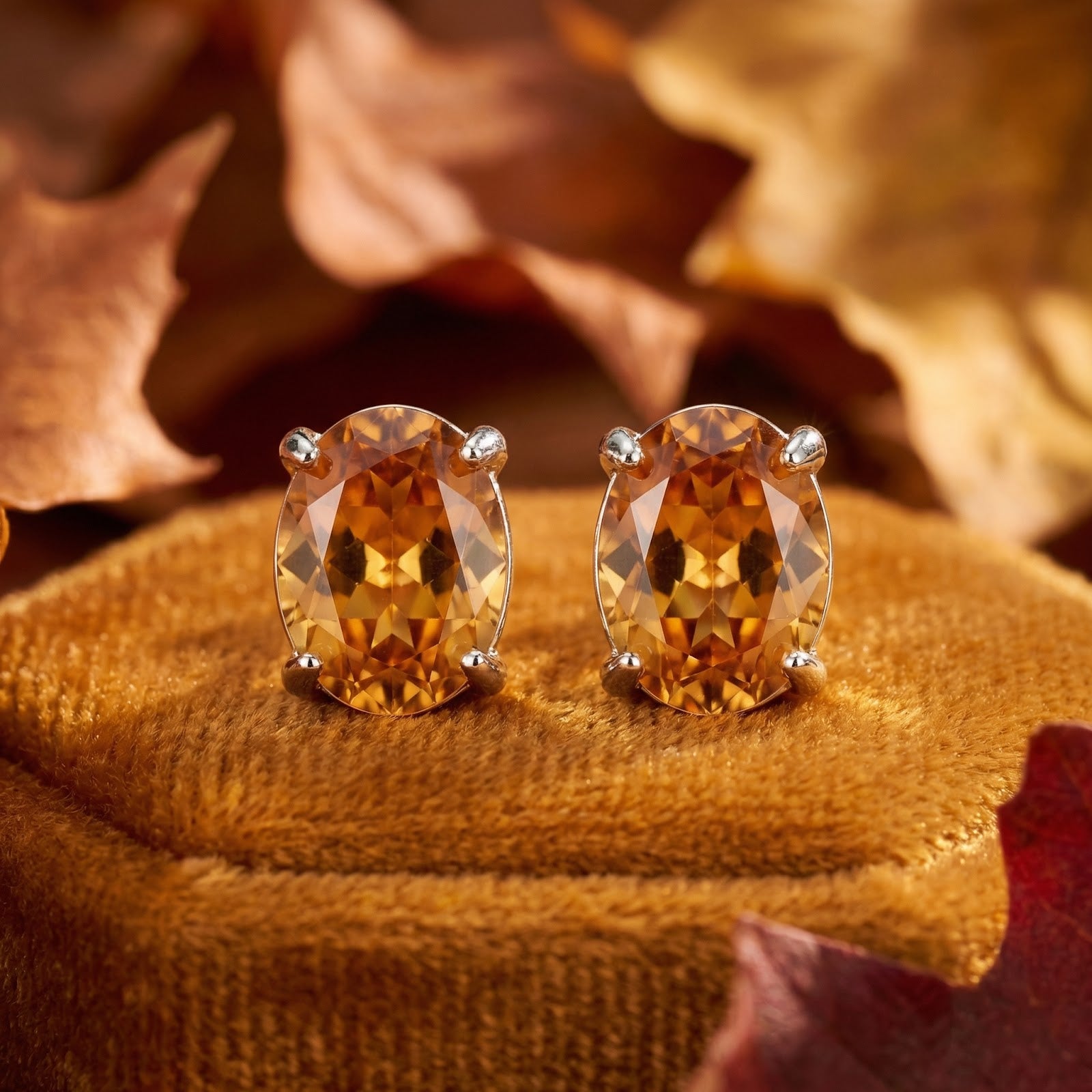 Macro view of oval cut honeyed simulated topaz stud earrings in silver four-prong settings.