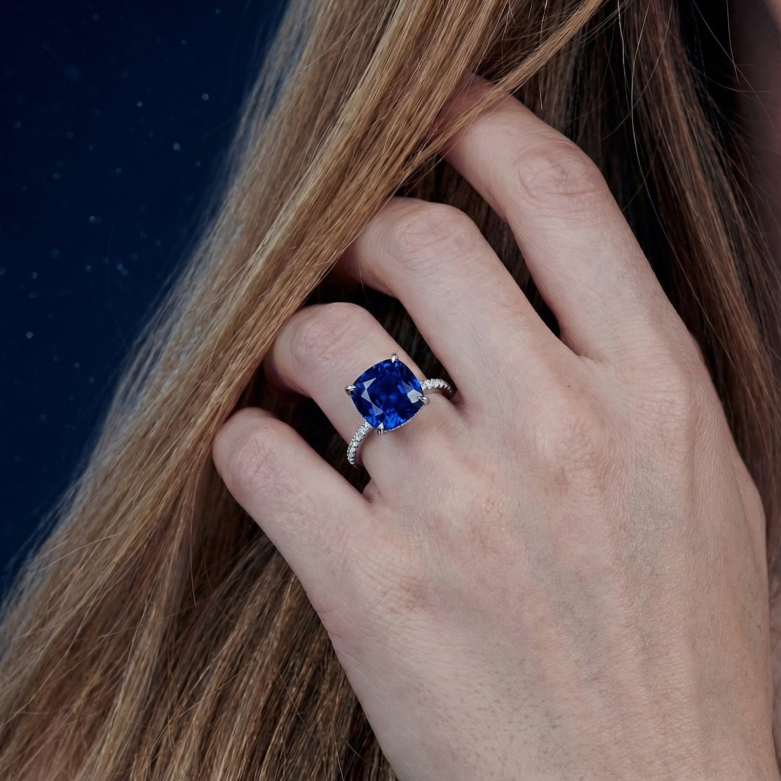 Close-up of a cushion cut blue sapphire sterling silver ring worn on a woman's hand.