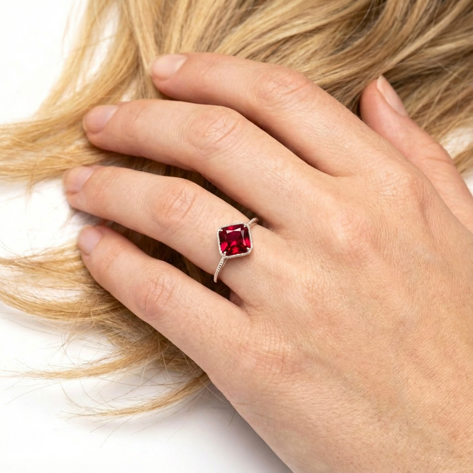 Square-cut simulated ruby sterling silver ring worn on a woman's hand against blonde hair.