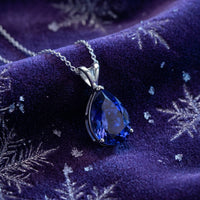 Pear-cut blue moissanite necklace resting on purple velvet with snowflake patterns.