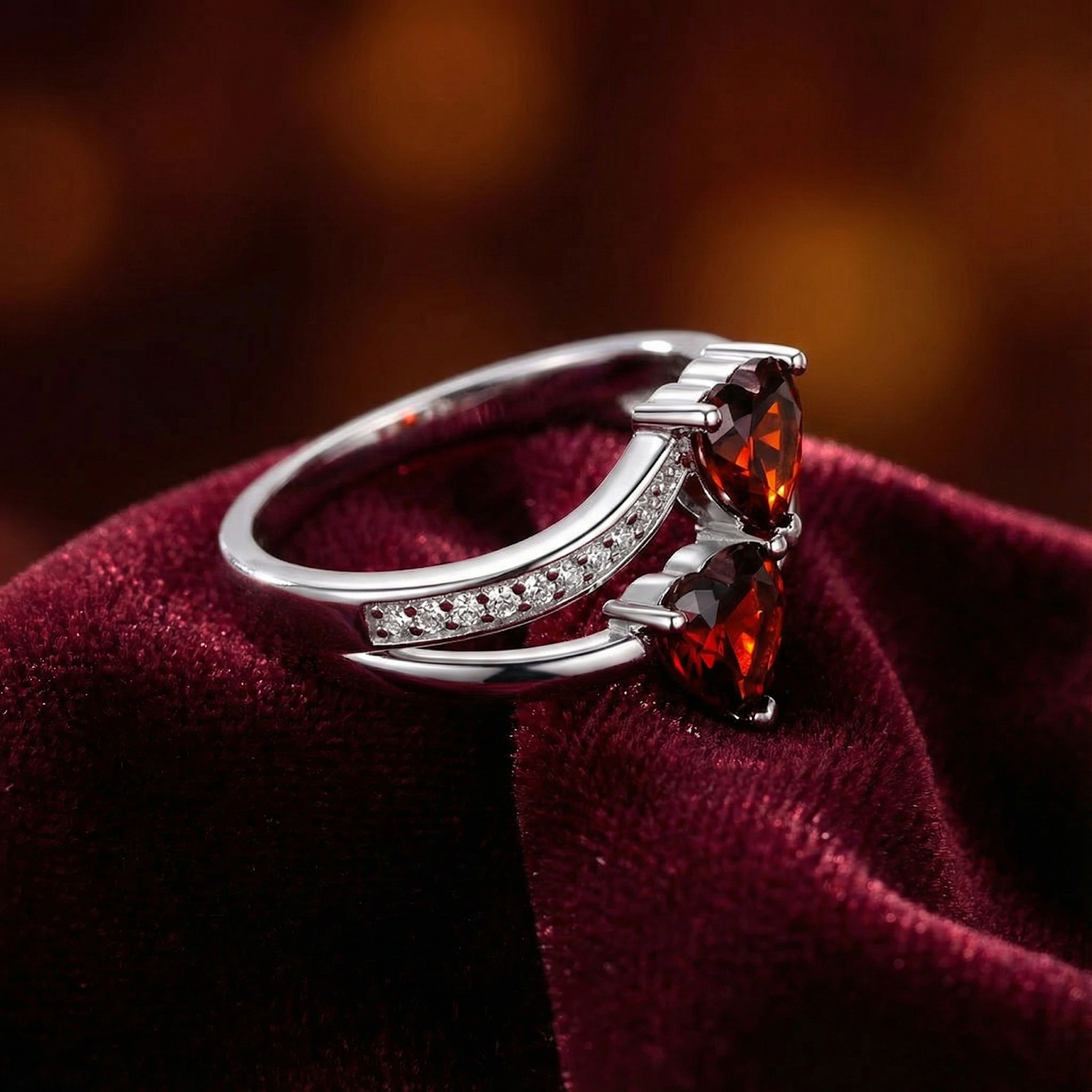 Side view of a sterling silver ring featuring two heart cut red simulated garnet stones on red velvet.