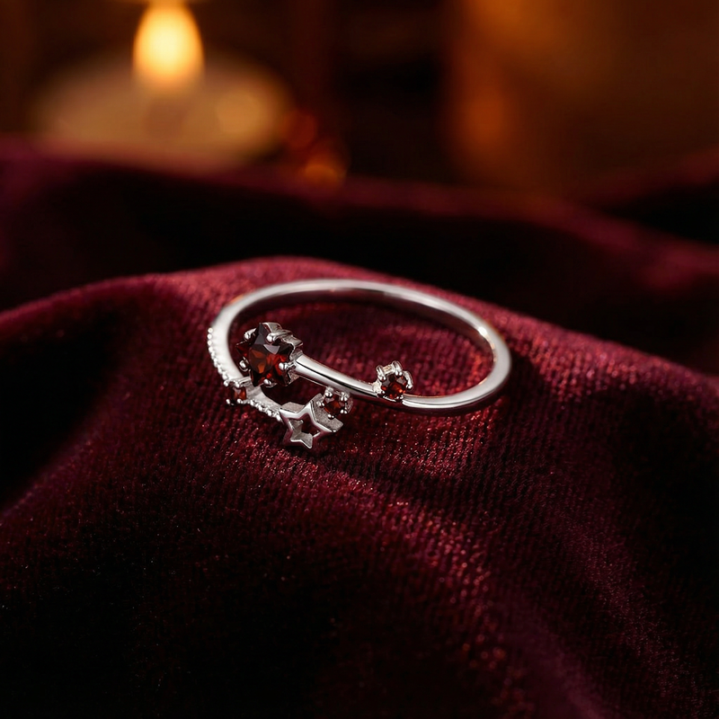 Adjustable sterling silver star ring with red simulated garnets resting on draped burgundy velvet.