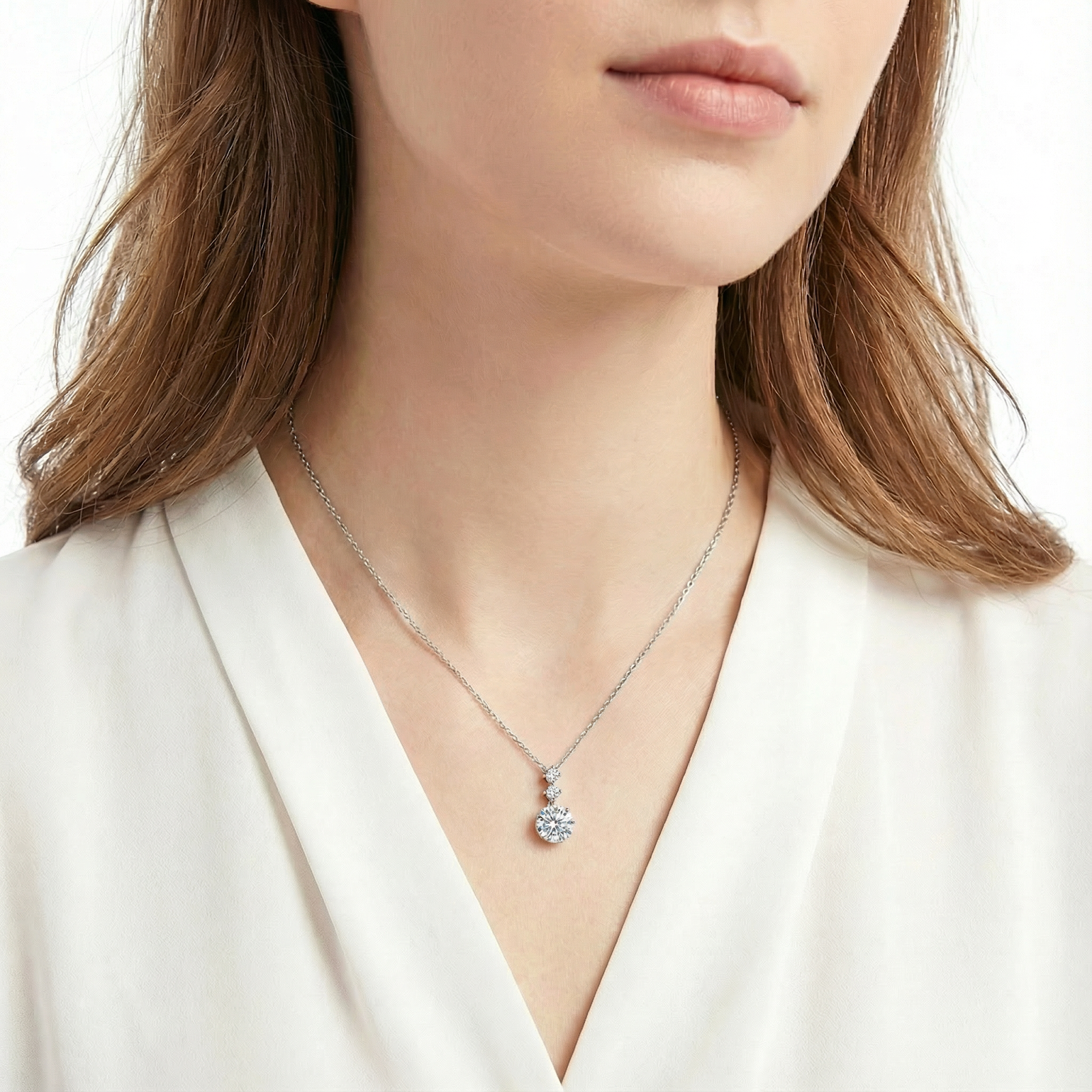 Woman wearing the Aurelle Drop sterling silver necklace with a three-stone simulated diamond pendant.