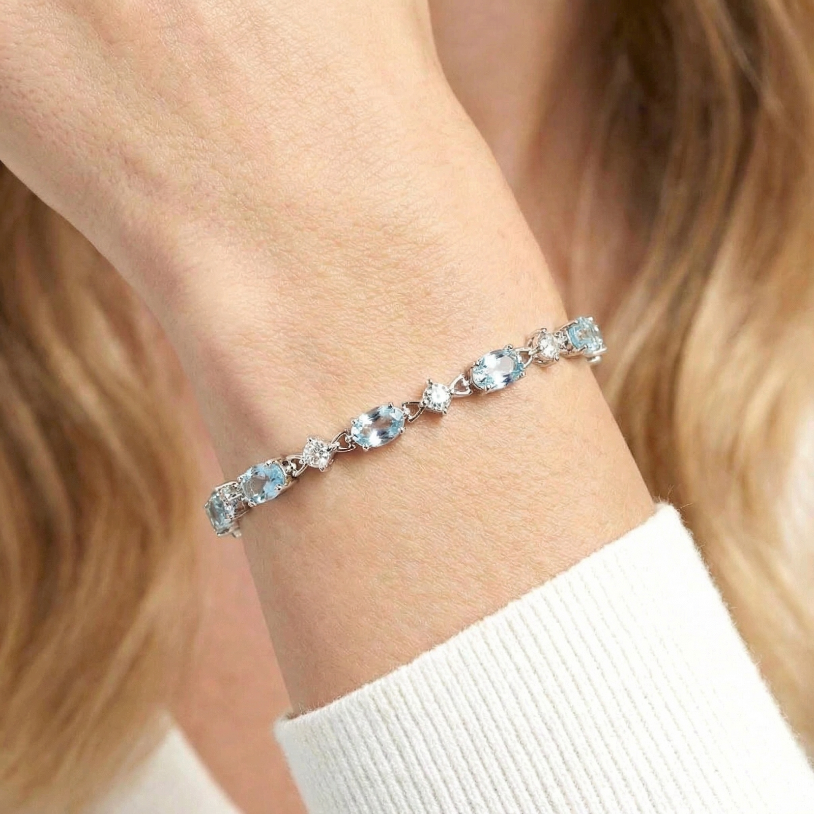 Close-up of oval-cut light blue simulated aquamarine stones in a sterling silver station bracelet on a wrist.