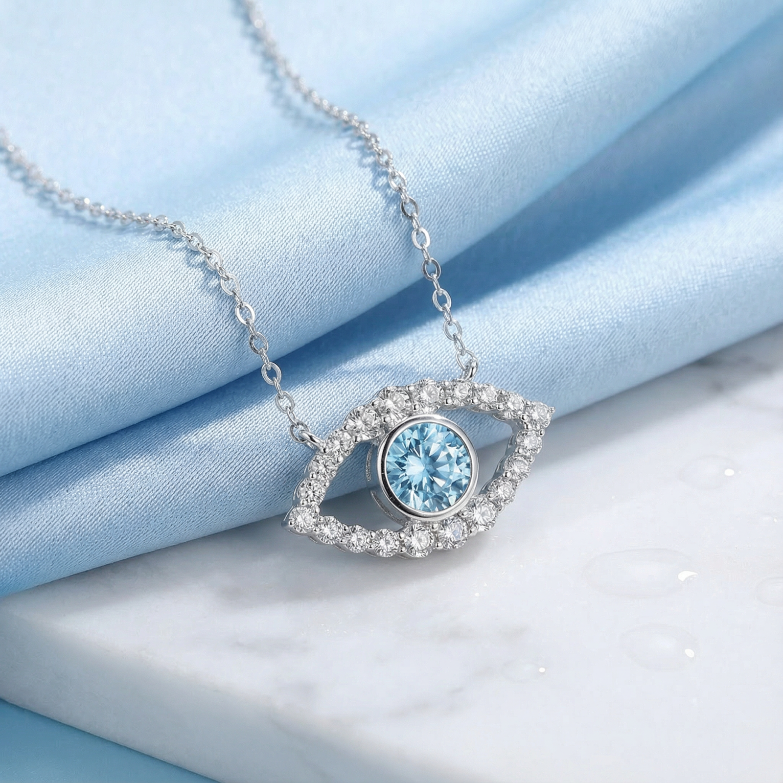 March birthstone eye necklace in sterling silver with round cut simulated aquamarine on blue silk and marble.