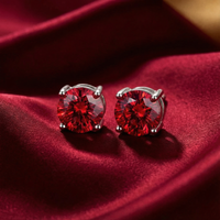 Round cut simulated ruby stud earrings in solid gold settings on a red silk background.
