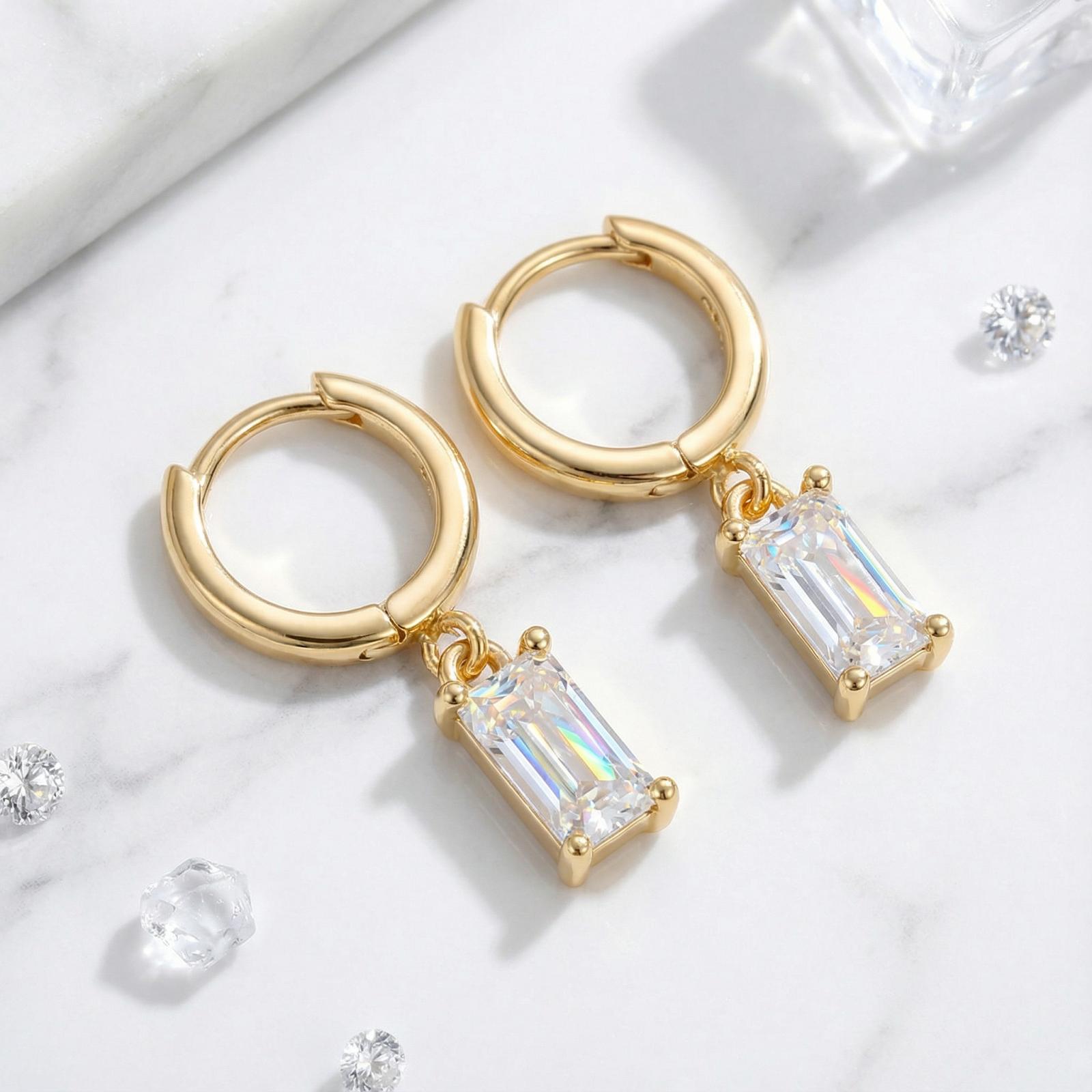 18K gold vermeil hoop earrings with emerald cut simulated diamonds on a white marble surface.