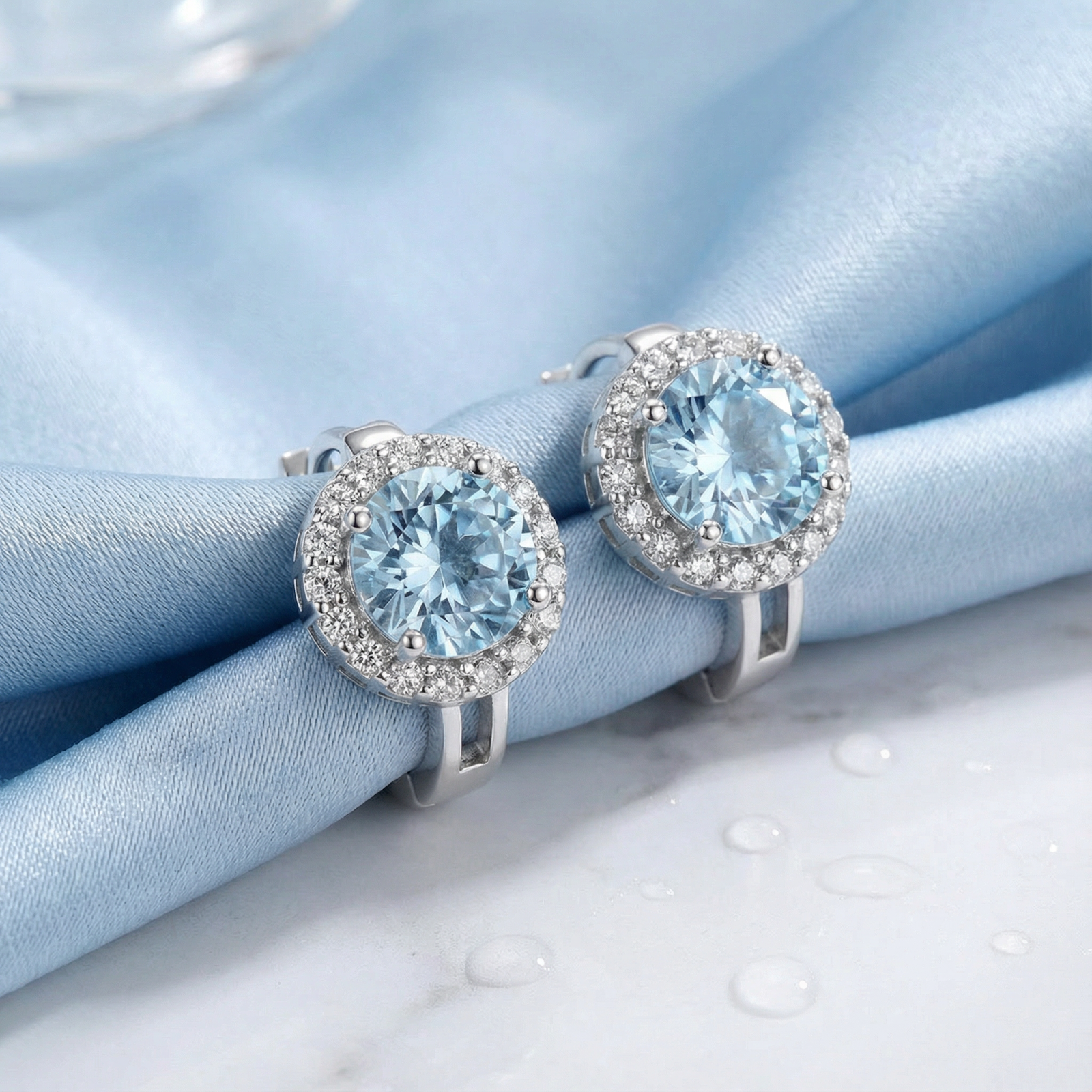 Round cut light blue simulated aquamarine halo drop earrings in sterling silver on blue silk fabric.