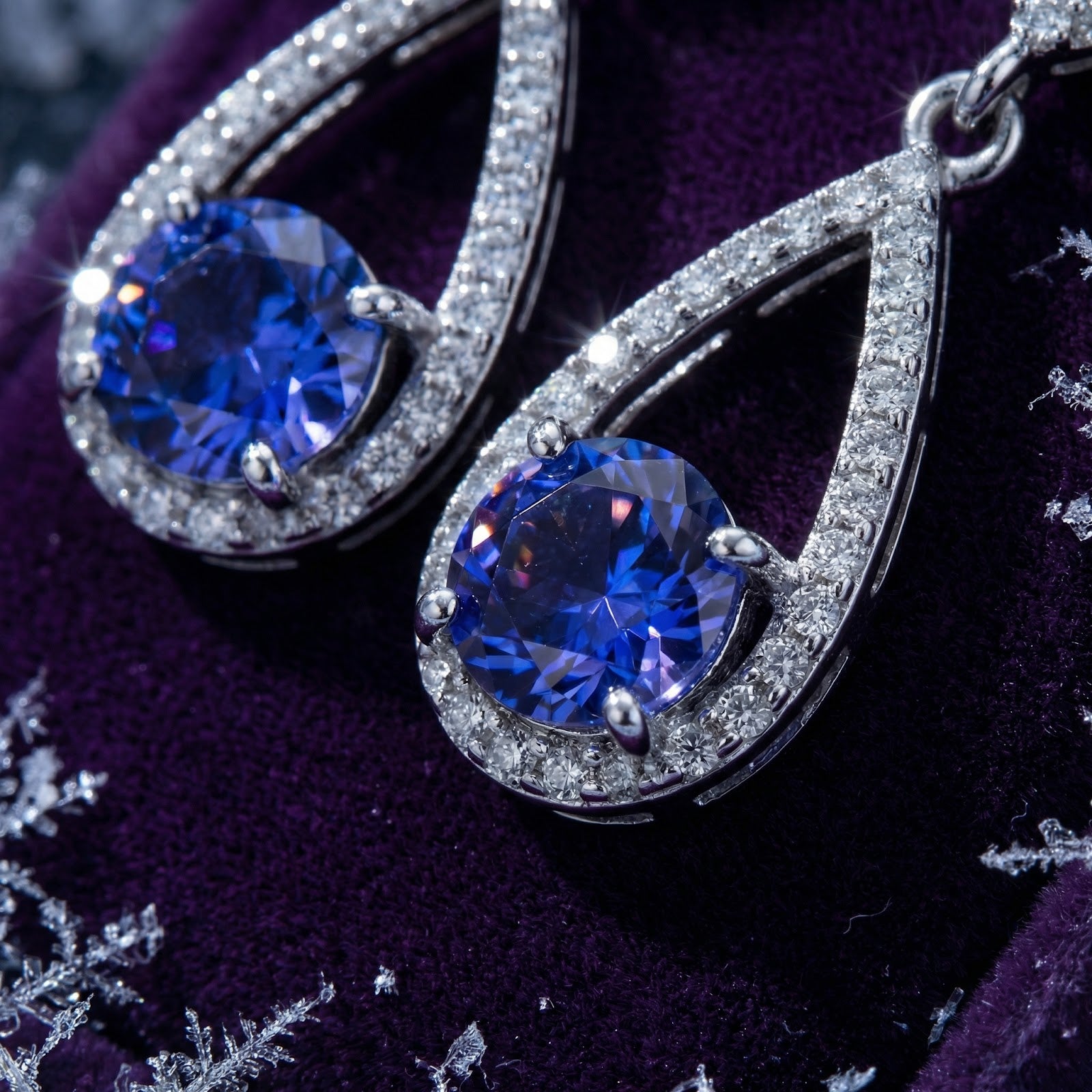 Macro view of sterling silver teardrop earrings with round blue simulated tanzanite on purple velvet.