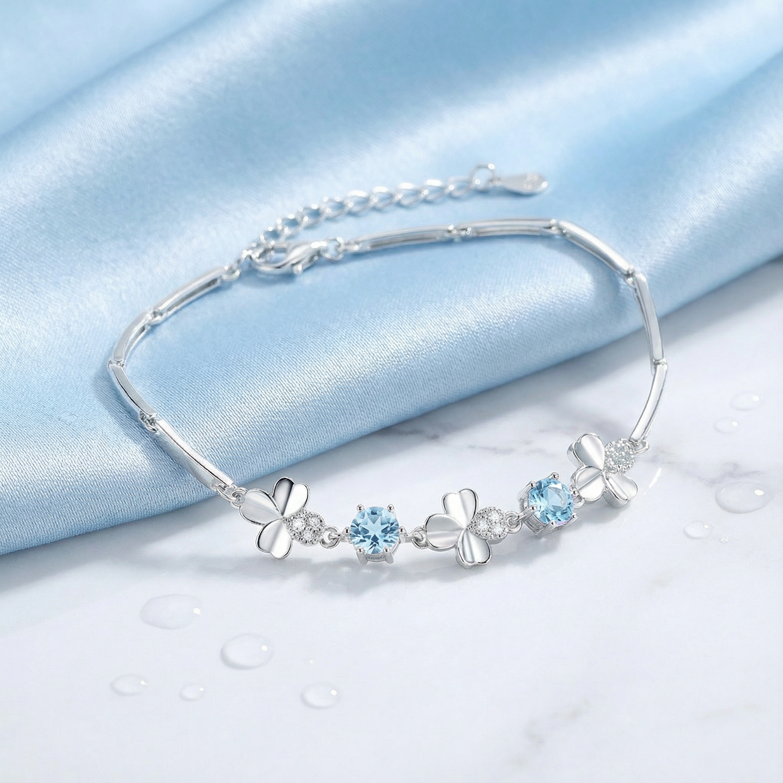 Sterling silver station bracelet with round simulated aquamarine and clover motifs on blue silk and marble.