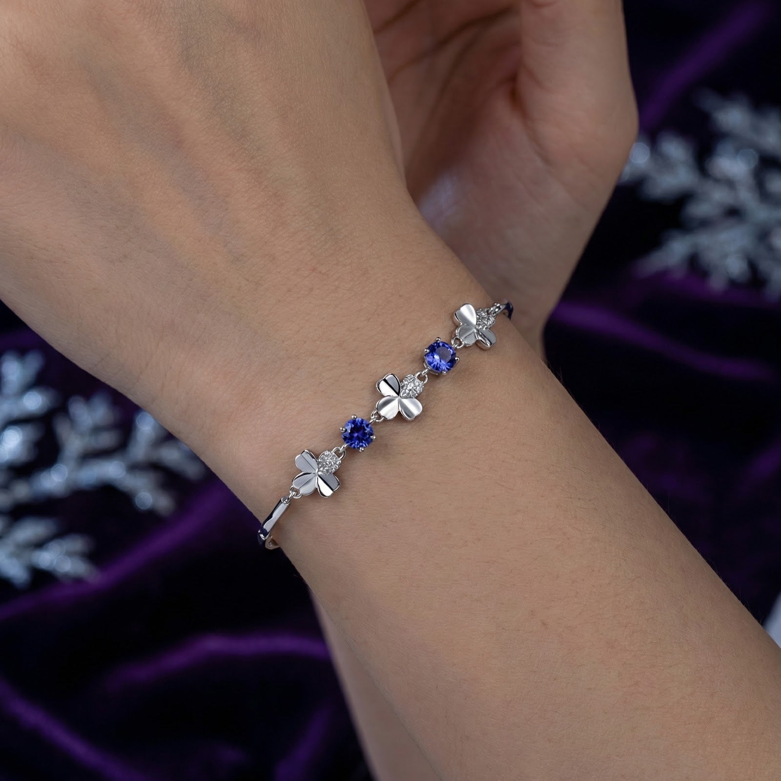 Detailed view of the silver clover bracelet with round blue simulated tanzanite stones worn on a wrist.