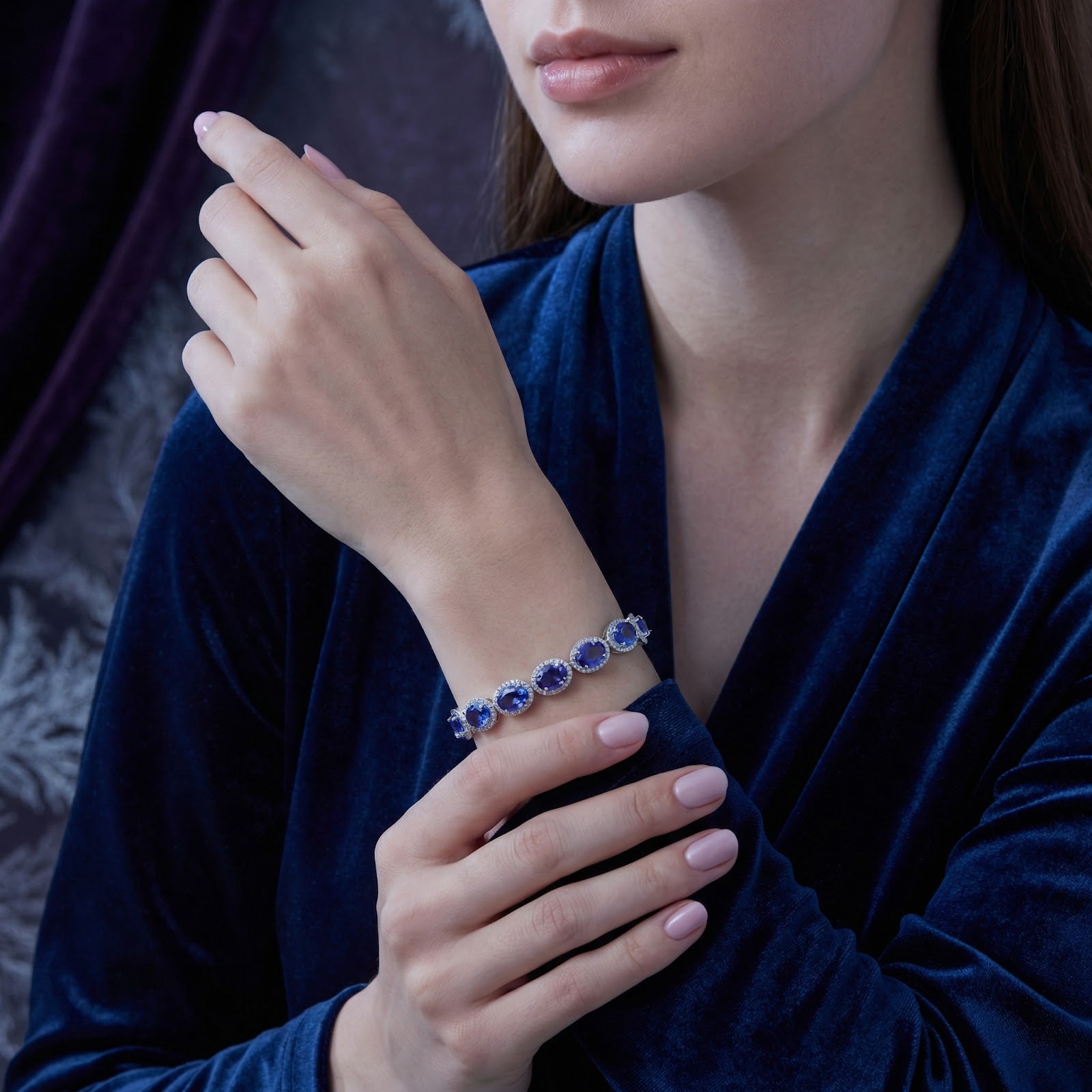 Sterling silver tennis bracelet with oval simulated tanzanite worn by a model in a blue velvet dress.