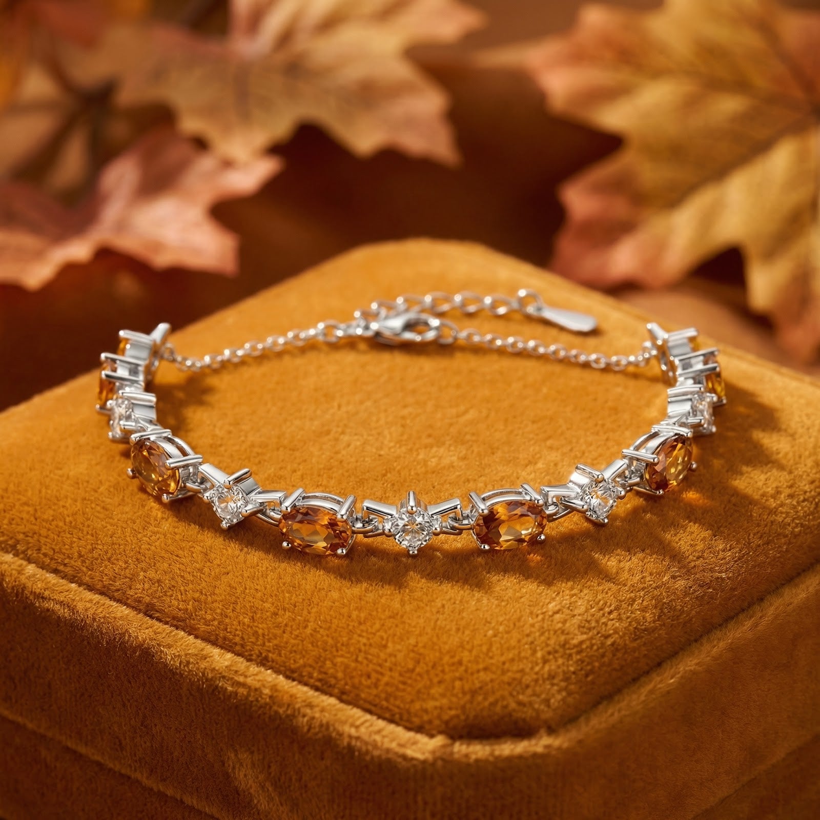 Sterling silver bracelet with oval honeyed topaz and round white stones on an orange velvet box with autumn leaves.