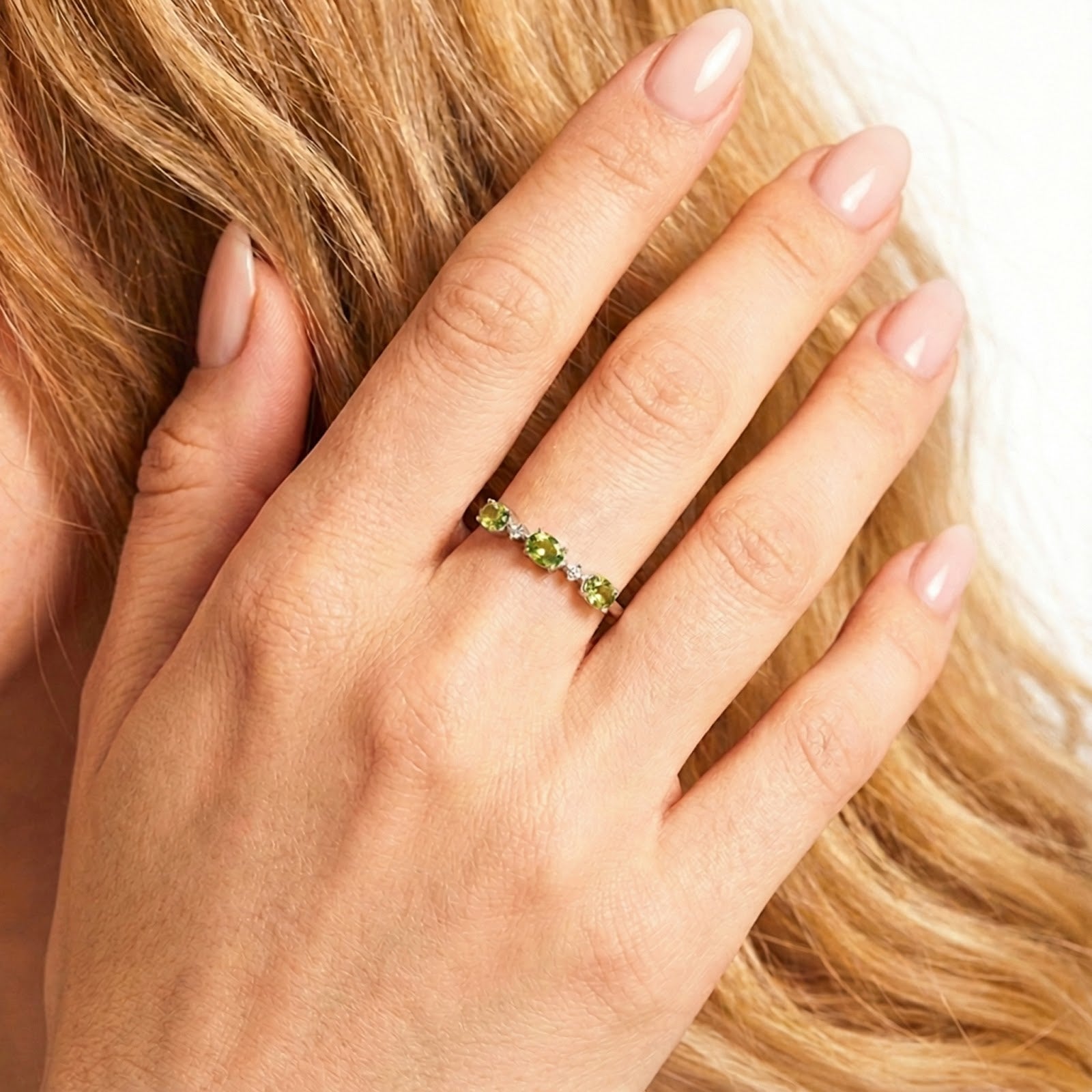 Close-up of the Mirabelle S925 sterling silver ring with oval simulated peridots worn on a hand touching hair.