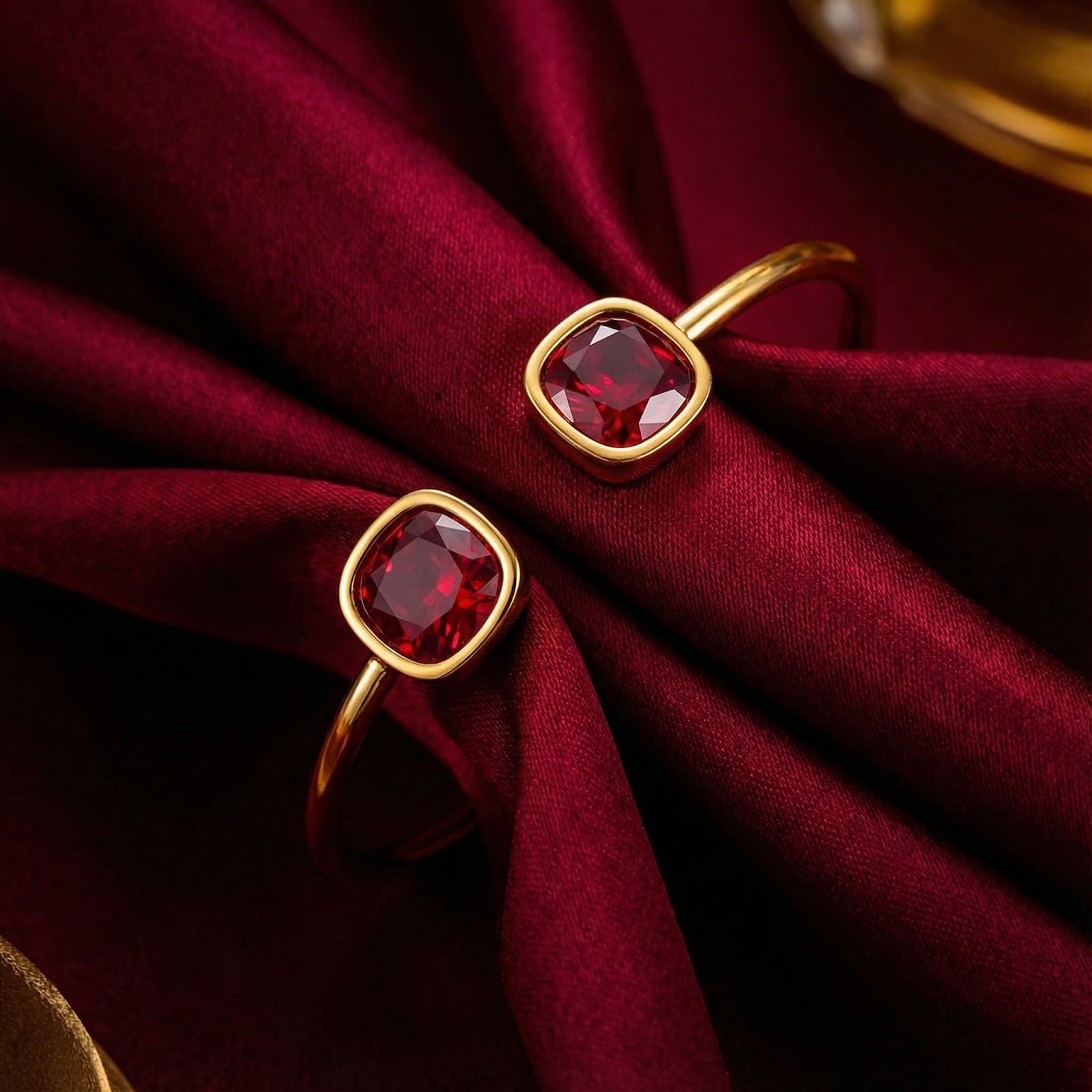 Close-up of cushion-cut simulated rubies in gold-tone settings on a stainless steel cuff bracelet.