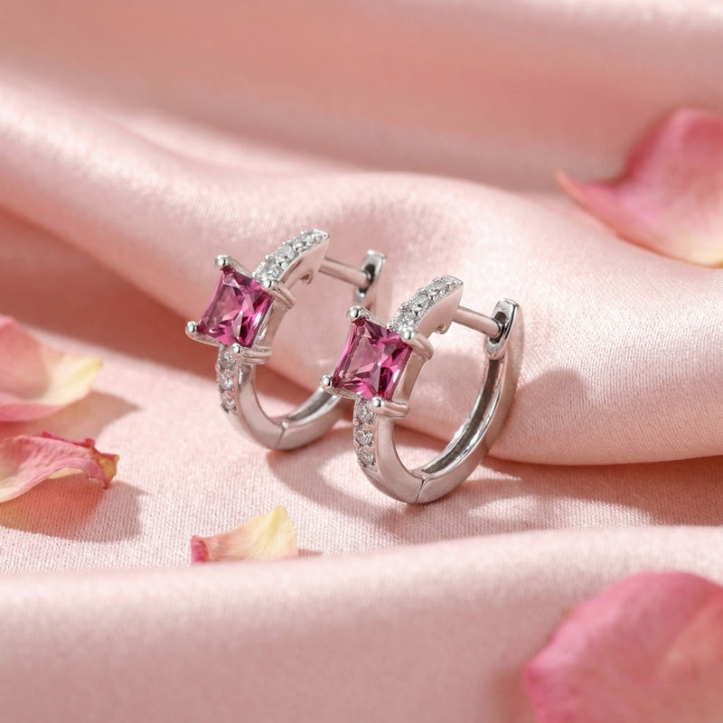 Side view of silver huggie earrings with square-cut pink tourmaline stones on pink fabric with rose petals.