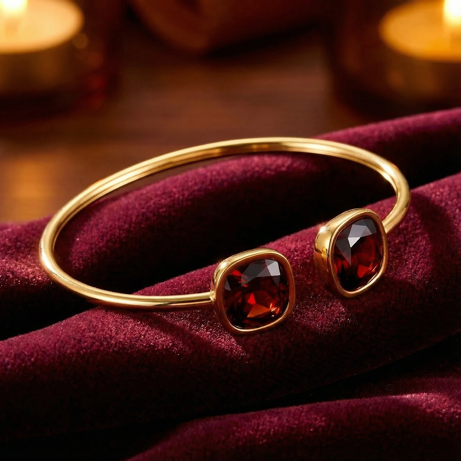 Gold stainless steel cuff bangle with square cushion-cut simulated garnets on red velvet with candlelight.