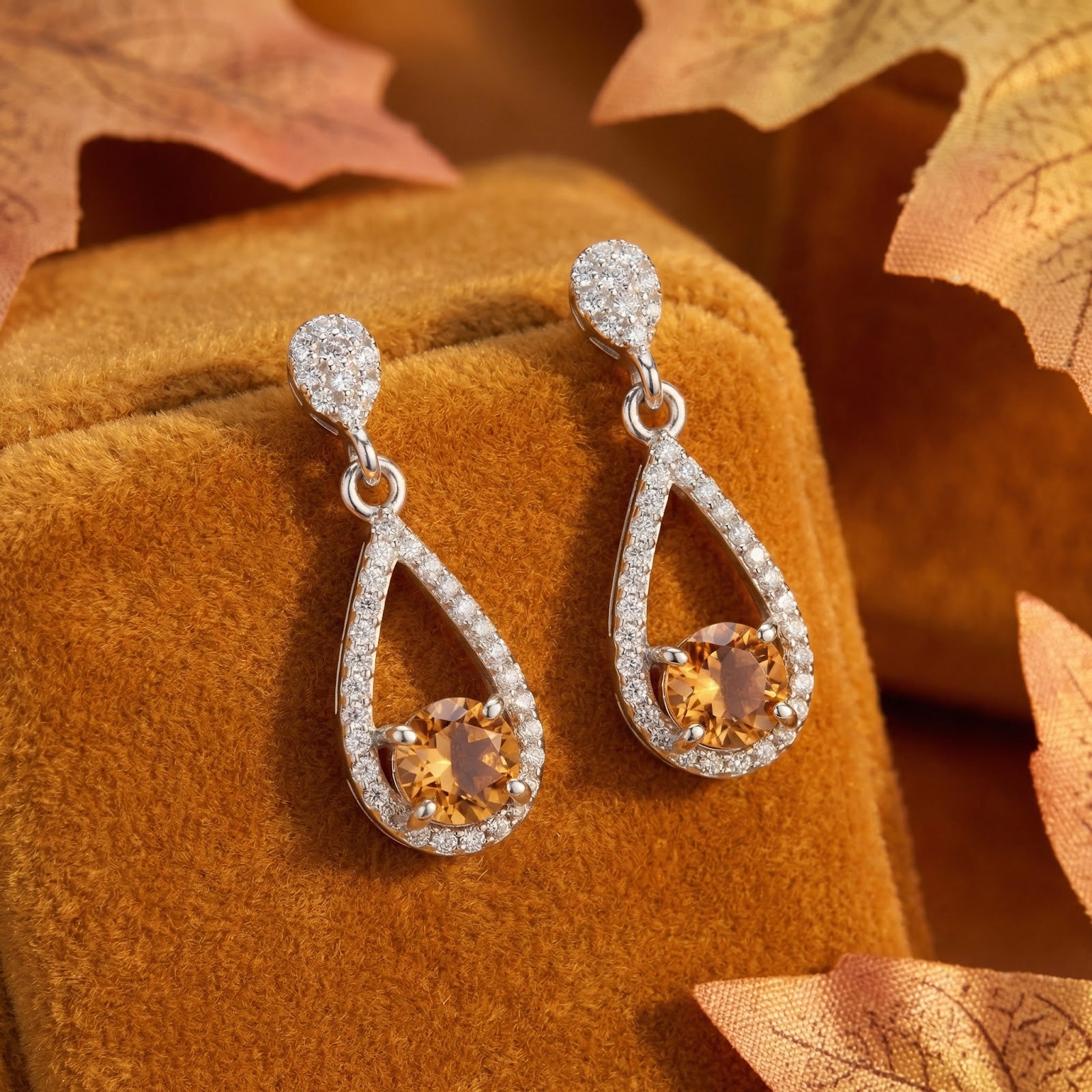 S925 sterling silver drop earrings with round-cut simulated topaz in a pear halo, styled with autumn leaves.