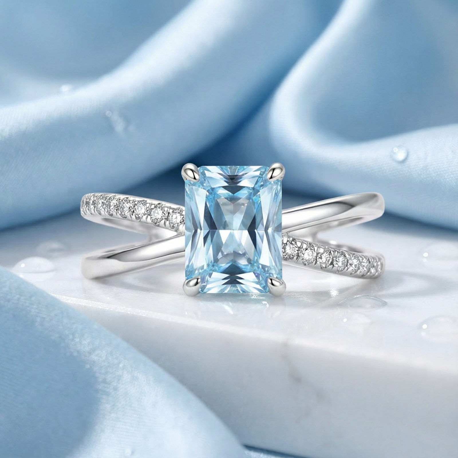 Emerald cut simulated aquamarine ring in S925 sterling silver with a twist band on blue fabric.