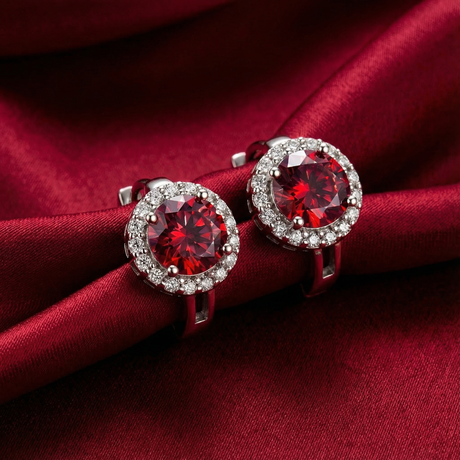 Round cut simulated ruby halo earrings in S925 sterling silver resting on red silk fabric.