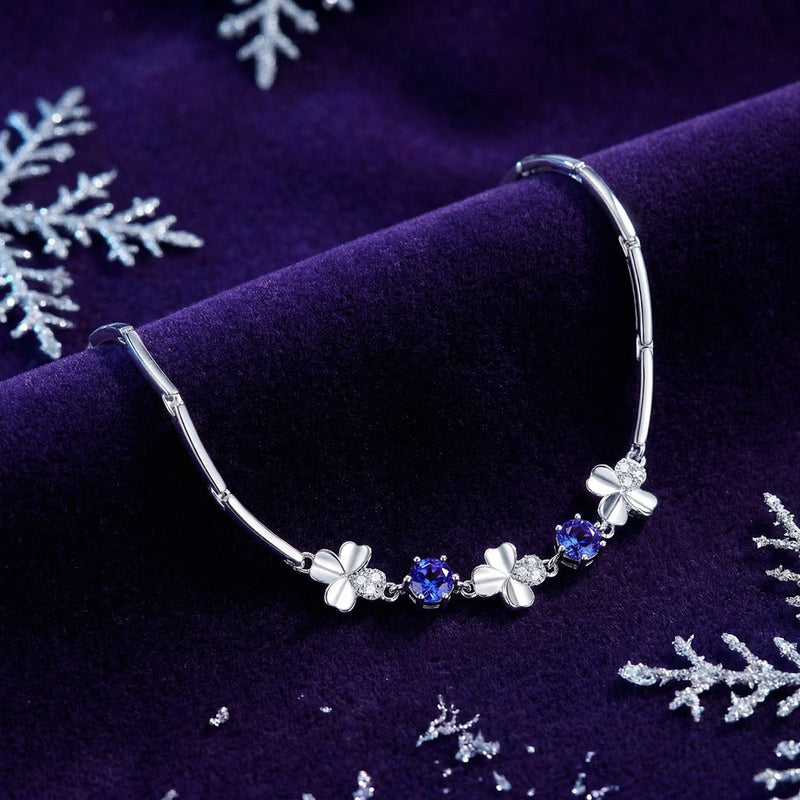 Close-up of silver clover charms and round blue simulated tanzanite stones on a purple velvet background.