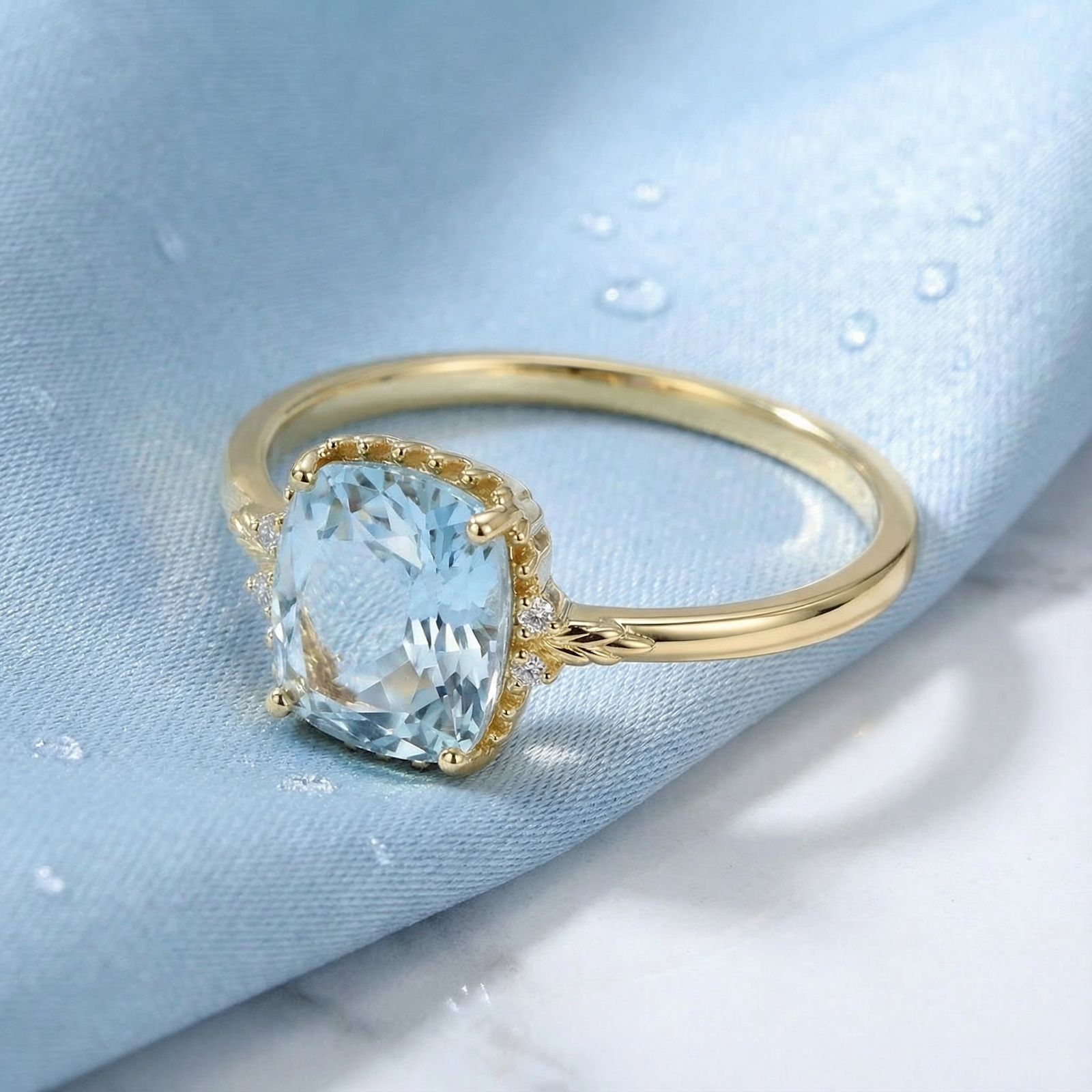 Cushion cut simulated aquamarine ring in 18K gold vermeil shown on light blue silk with water droplets.