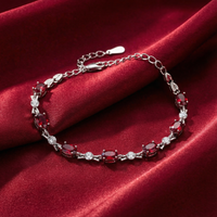 The Vivara oval-cut simulated ruby tennis bracelet in solid gold on a red silk background.