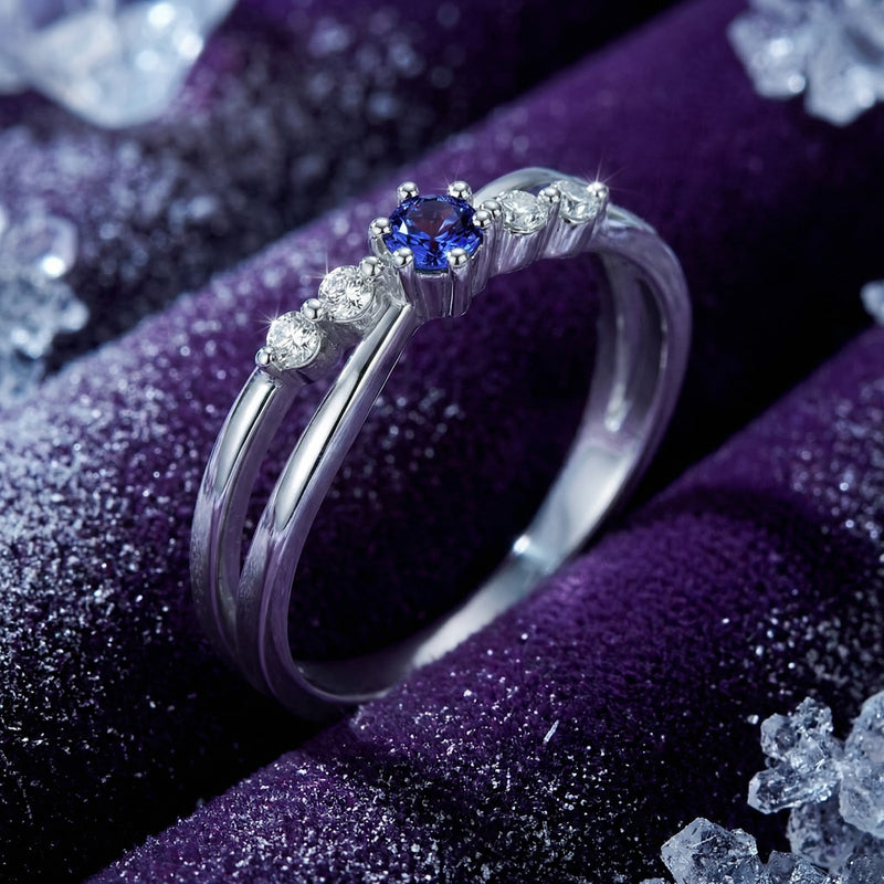 Macro view of the round-cut simulated tanzanite and side stones on an S925 sterling silver crossover ring.