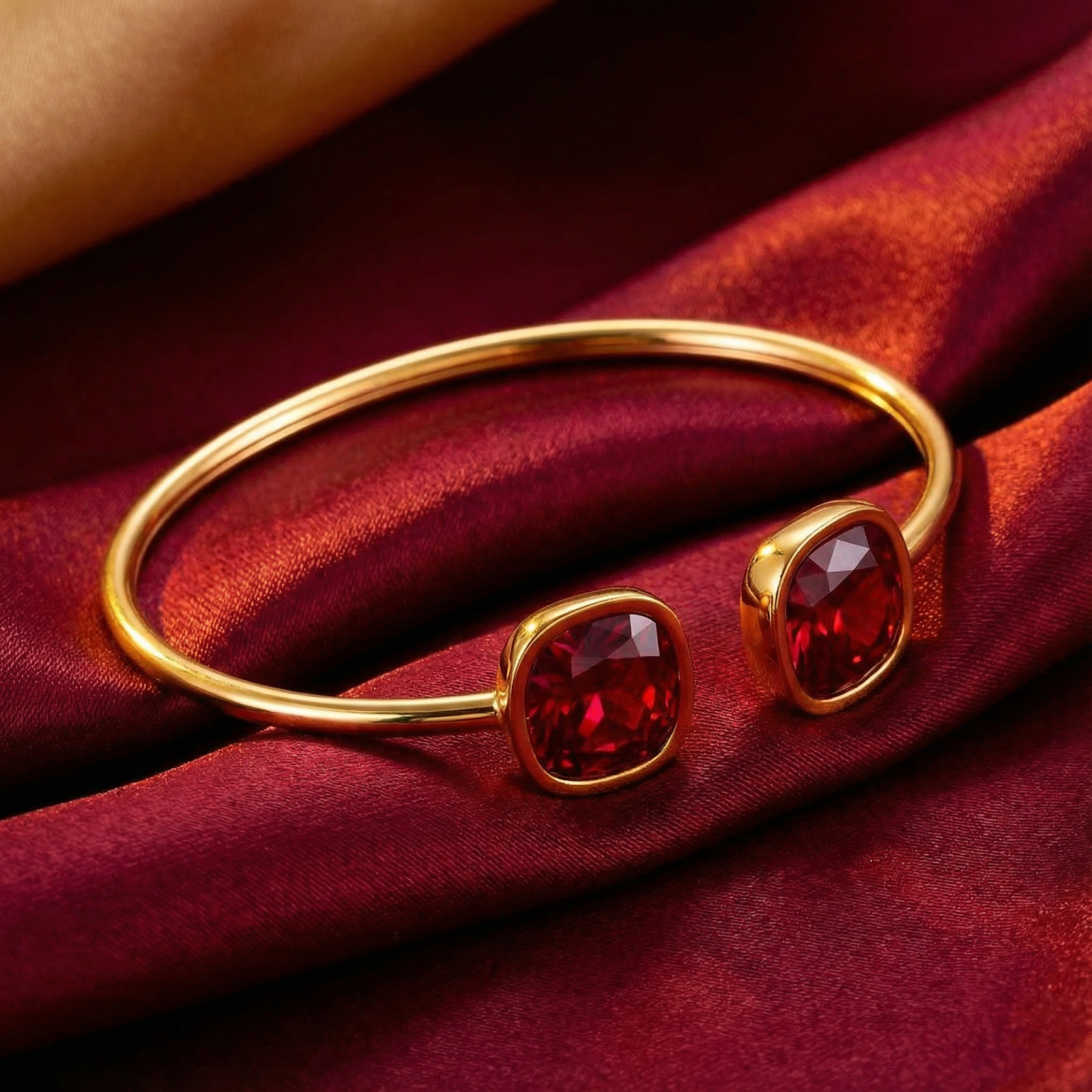 Gold-tone stainless steel cuff bracelet with cushion-cut simulated rubies on red silk fabric.