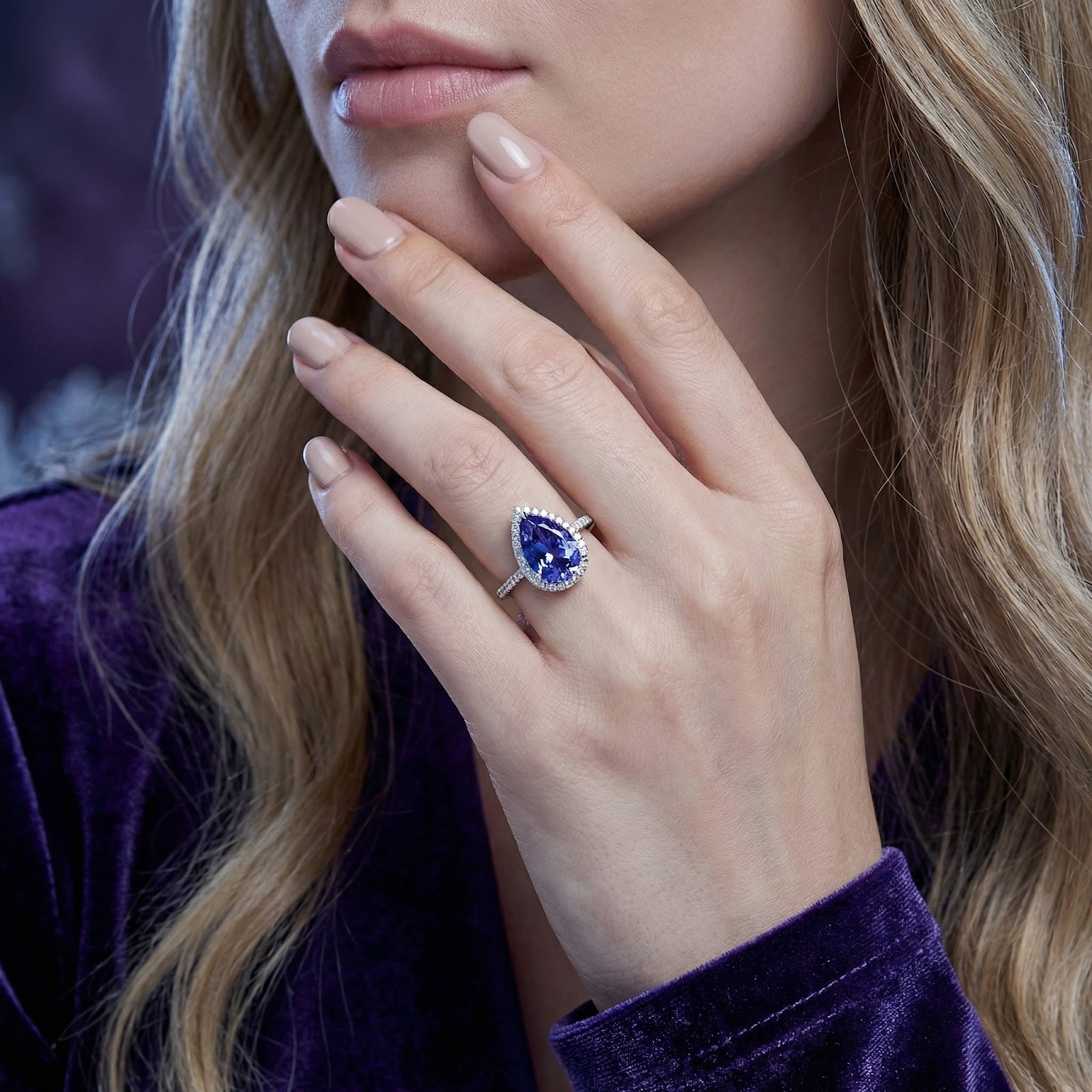 Zenelle pear cut simulated tanzanite ring in S925 sterling silver worn on a woman's hand near her face.