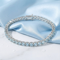 Round cut simulated aquamarine tennis bracelet in solid gold on light blue silk with water droplets.