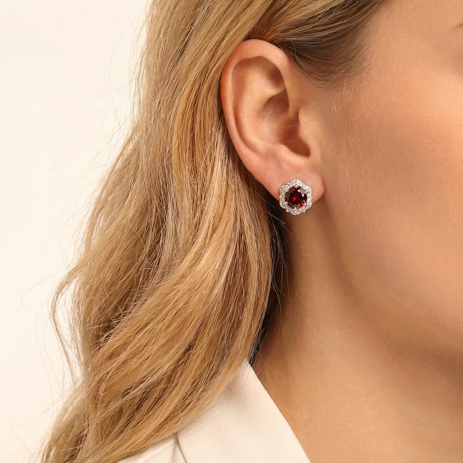 Woman wearing a sterling silver halo stud earring with a round red simulated garnet on her earlobe.