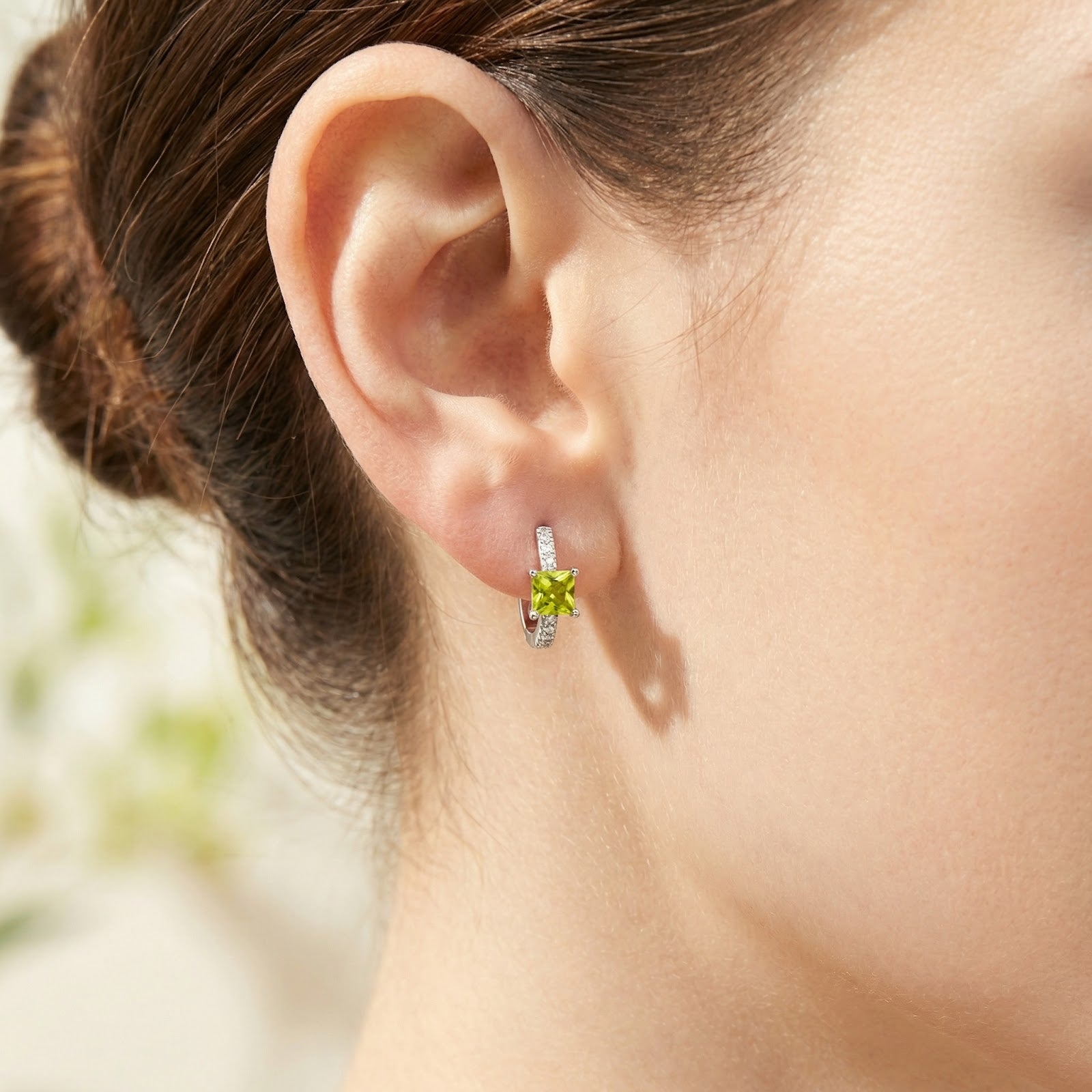 Close-up of a square-cut simulated peridot sterling silver earring worn on a woman's ear.