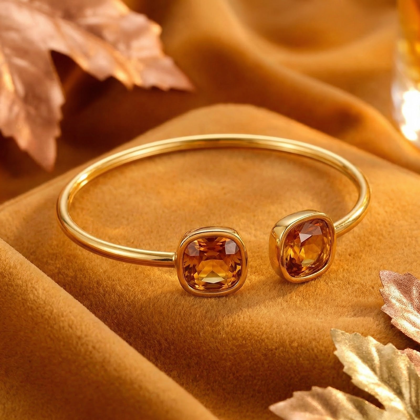 Gold-tone stainless steel bangle featuring two cushion-cut simulated topaz stones on a warm velvet background.