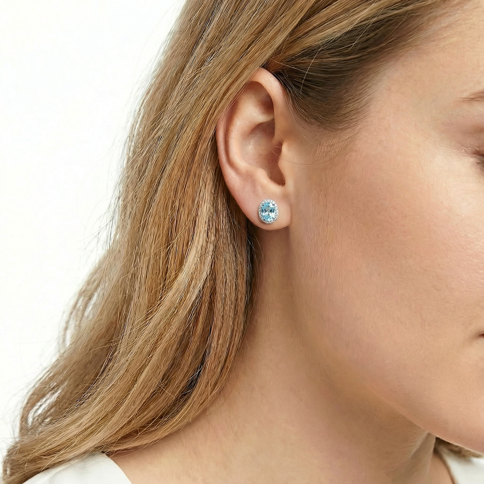 Side profile of a woman wearing the oval simulated aquamarine halo stud earrings in sterling silver.
