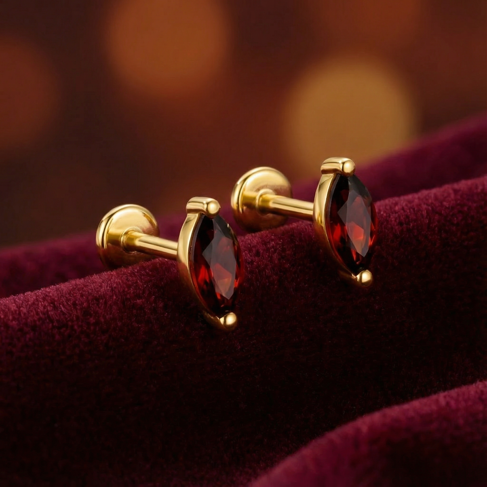 Side view of marquise cut simulated garnet stud earrings in 18K gold vermeil resting on red velvet.