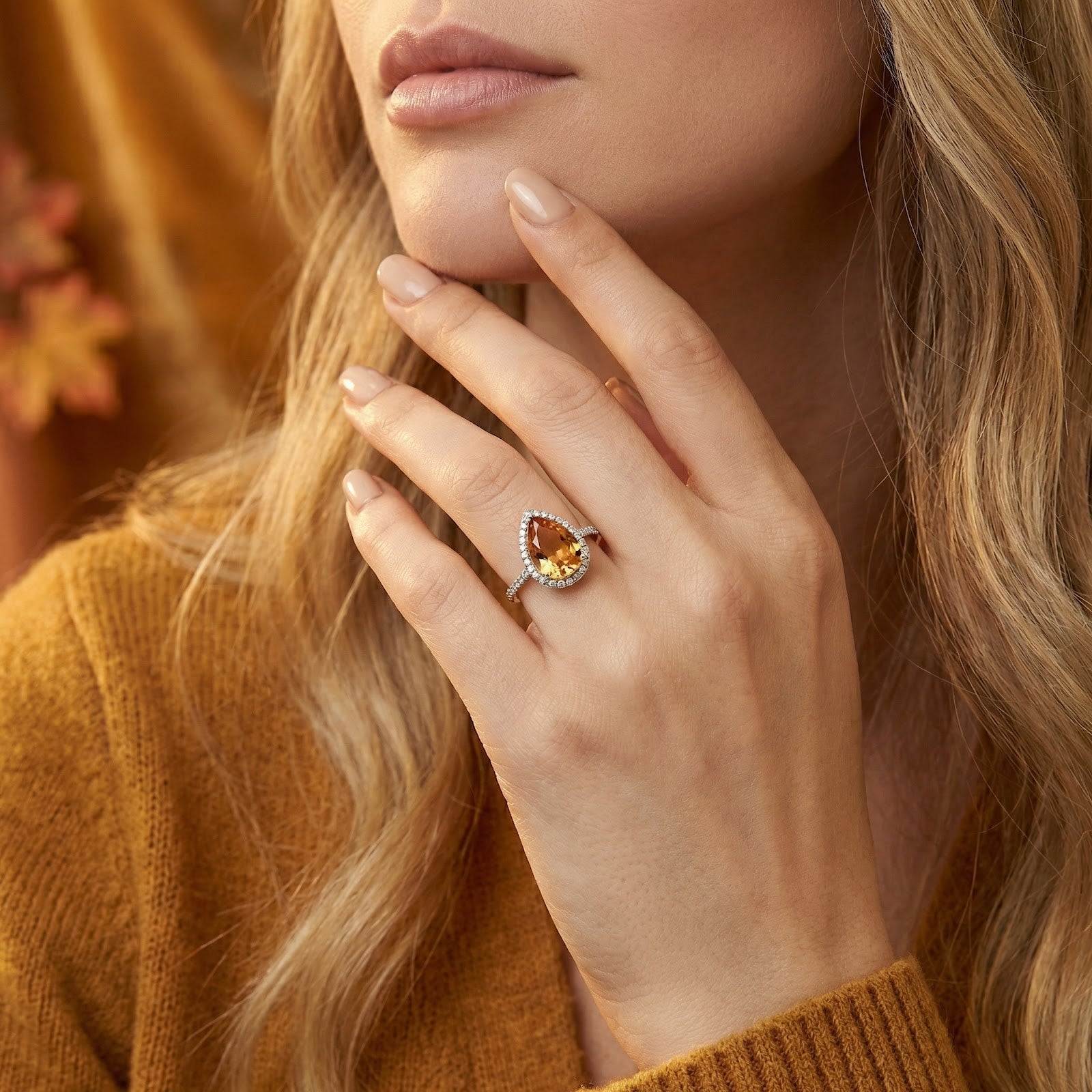 Woman wearing the pear-cut simulated topaz halo ring in sterling silver on her finger, hand held near her face.