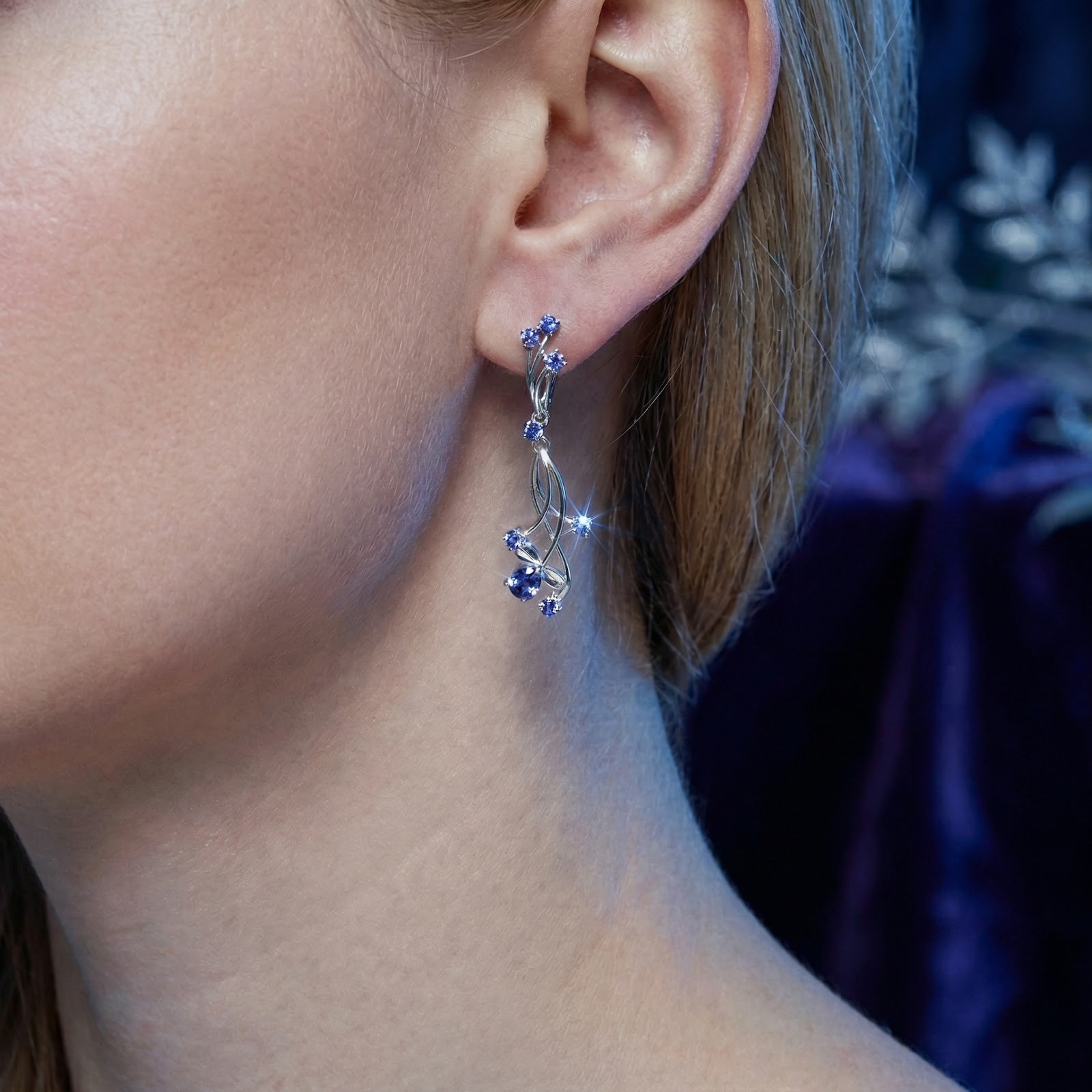 Macro view of a Thalinea sterling silver earring with pear-cut simulated tanzanite worn on a model's ear.