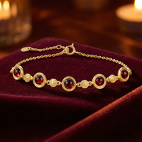 The Calyssa station bracelet in solid gold with round simulated garnets on a red velvet background.