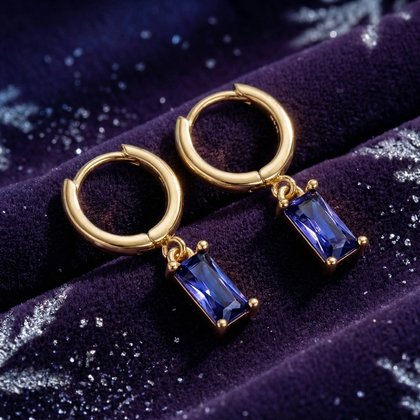 Emerald-cut simulated tanzanite drop earrings in 18K gold vermeil displayed on purple velvet with snowflakes.