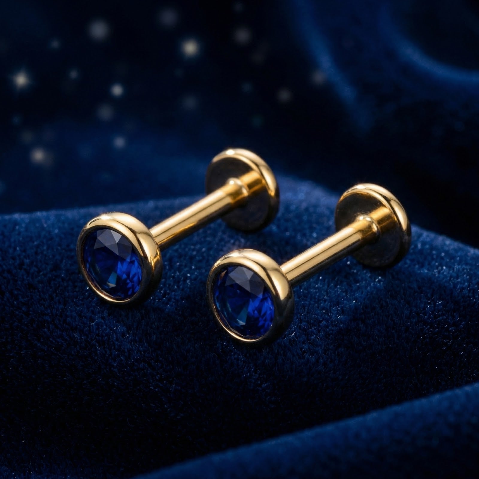 Round simulated sapphire bezel stud earrings in 18K gold vermeil, angled side view on blue velvet.