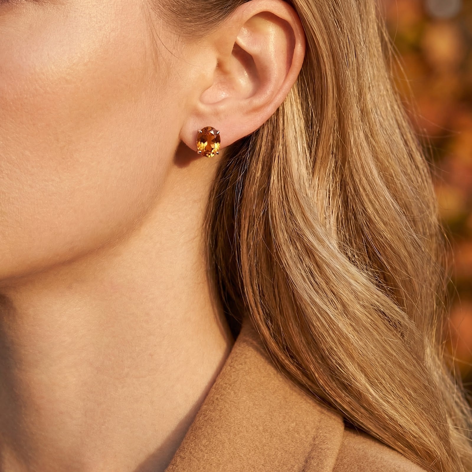 Side view of a model wearing an oval cut simulated topaz stud earring in sterling silver.