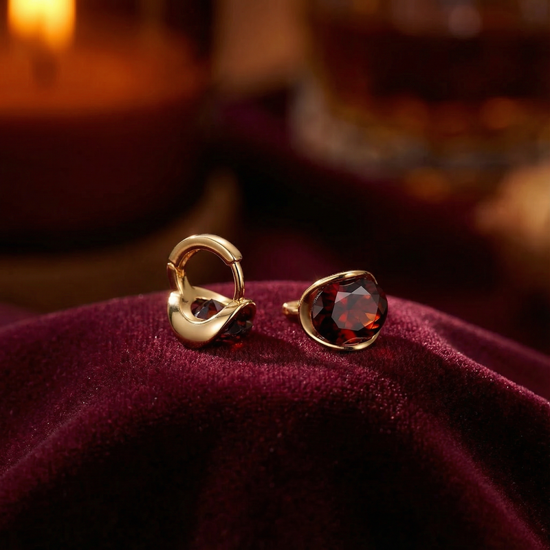 Close-up of 18K gold vermeil huggie earrings showing the round cut simulated garnet and hinge clasp.