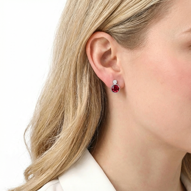 Close-up of a round cut simulated ruby stud earring in sterling silver worn on a woman's ear.
