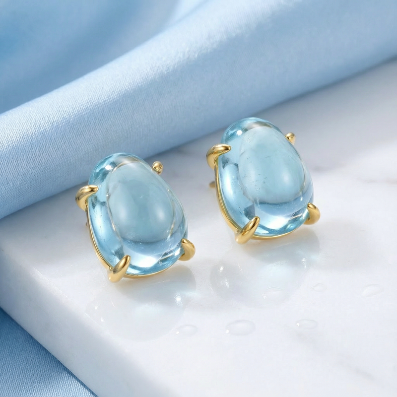 Angled view of organic cut March birthstone simulated aquamarine stud earrings in 18K gold vermeil on marble.