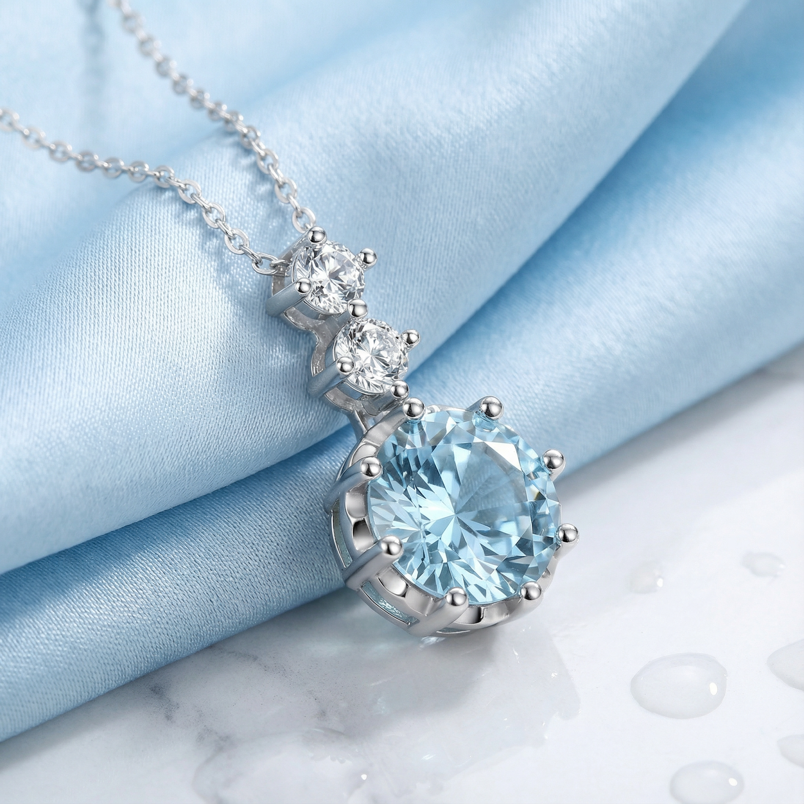 Round-cut simulated aquamarine necklace in sterling silver, styled on blue silk and marble with water droplets.