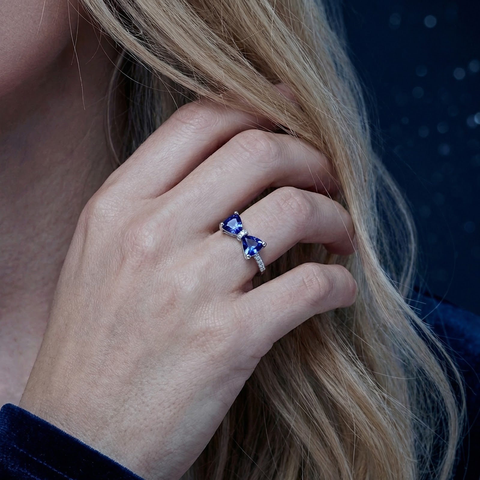 Close-up of the S925 sterling silver Marcelle bow ring with blue trillion-cut simulated sapphires worn on a hand.