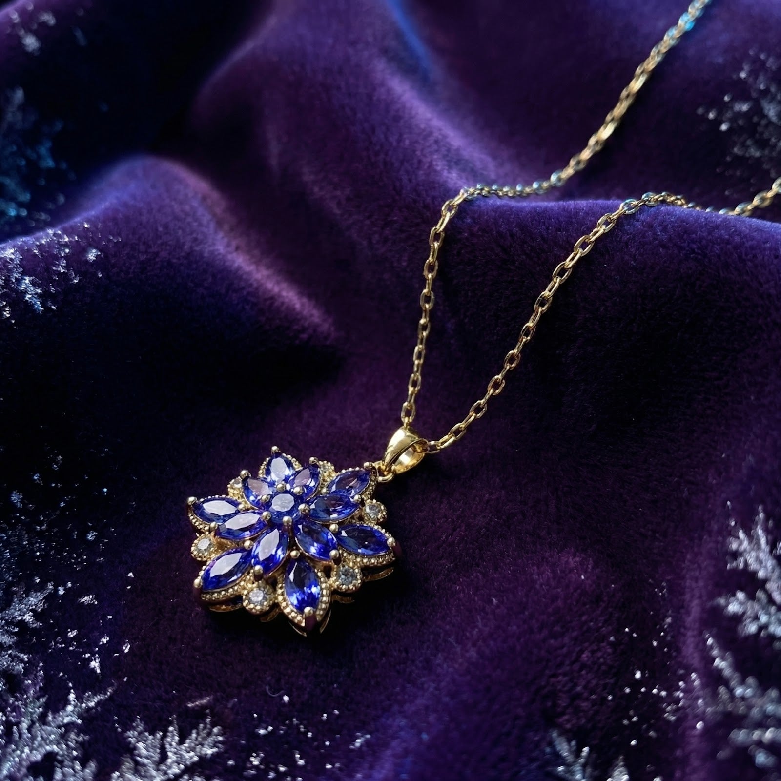 Close-up of the gold finish stainless steel tanzanite bloom necklace resting on purple velvet with snowflakes.