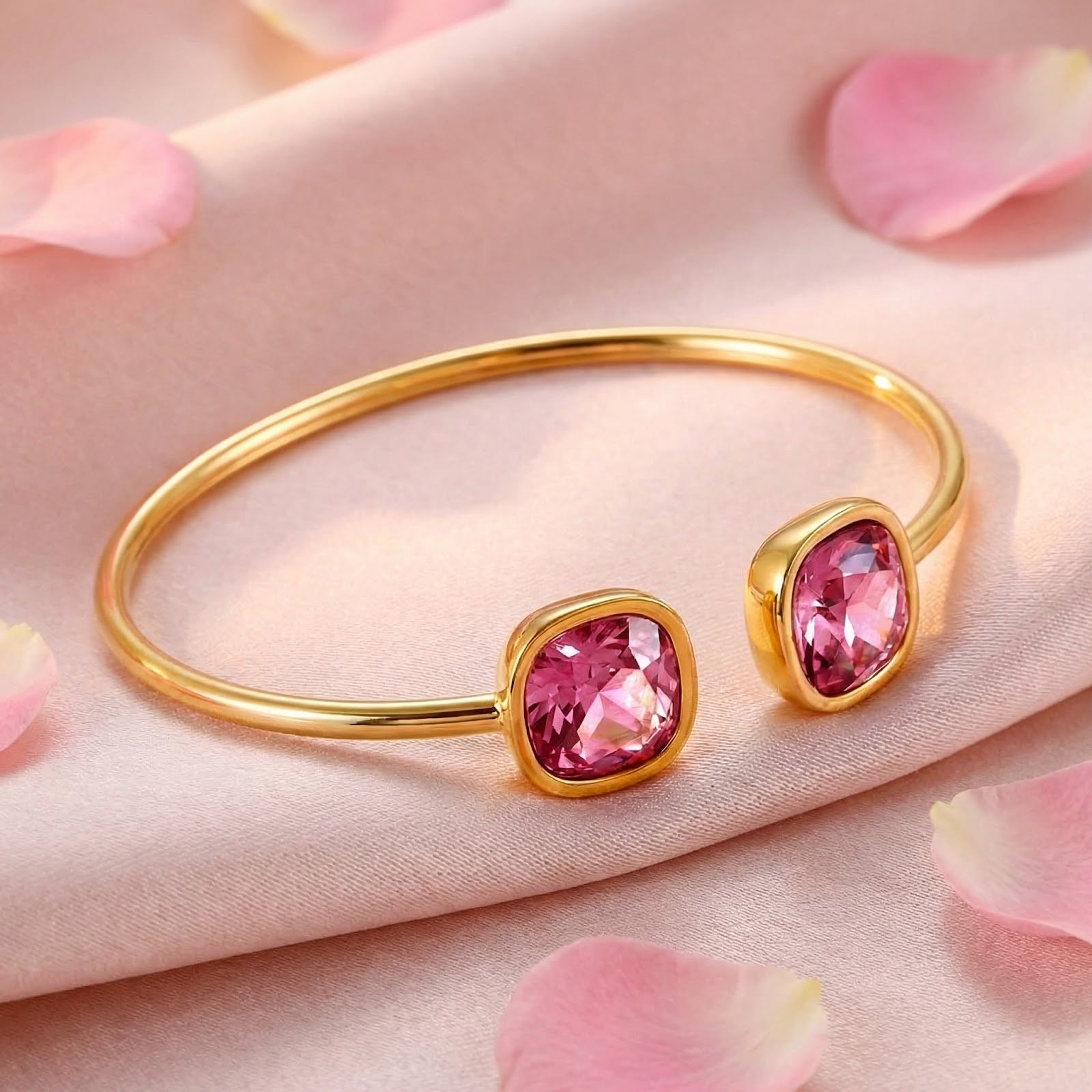 Angled view of a gold-toned stainless steel cuff with cushion-cut pink simulated tourmalines on pink silk with petals.