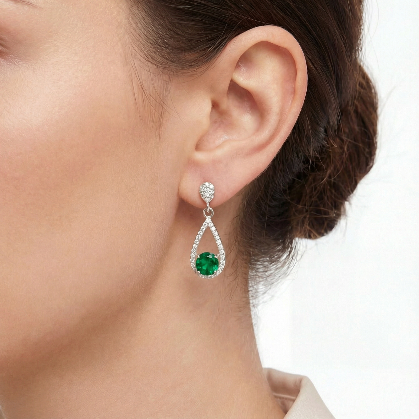 Close-up view of a sterling silver simulated emerald drop earring worn on a model's ear.
